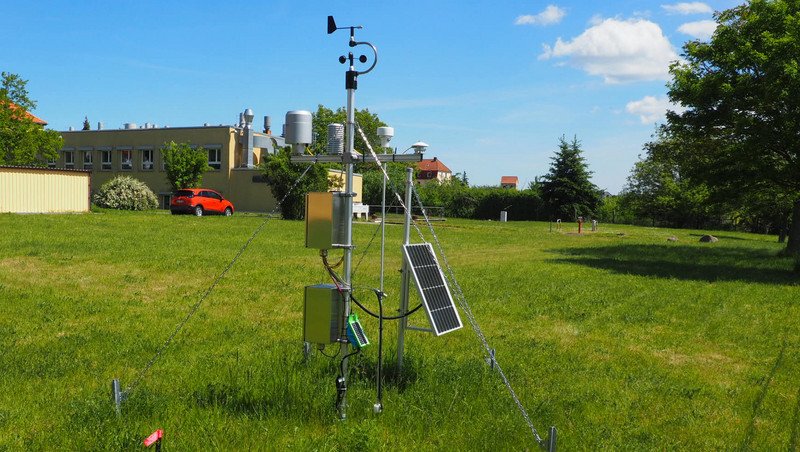 Zu sehen ist eine Wetterstation. Ein Gerüst aus Metall. Zirka einen Meter hoch. Es steht auf einer grünen Wiese. 